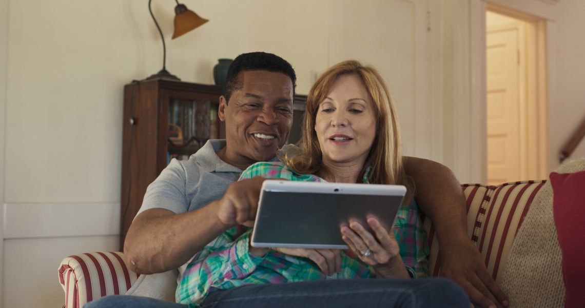 A biracial older couple cuddling together on a couch and using a tablet to research tax credits available to them.