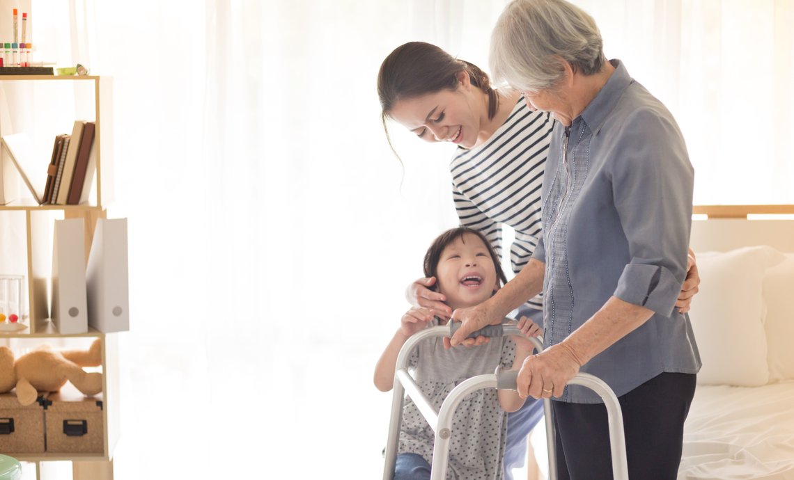 Older Asian woman with a walker receives assistance from middle-aged daughter and smiling granddaughter