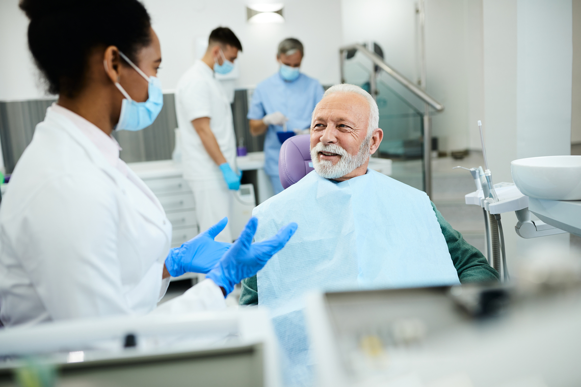 Dentist sharing good news with an older patient about their dental checkup results. The patient is in the dental chair and is smiling.