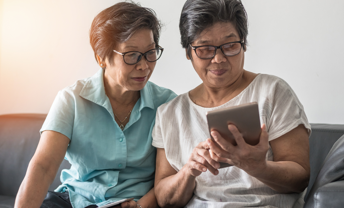 Same-gender older couple sitting on a couch and looking at a tablet together.