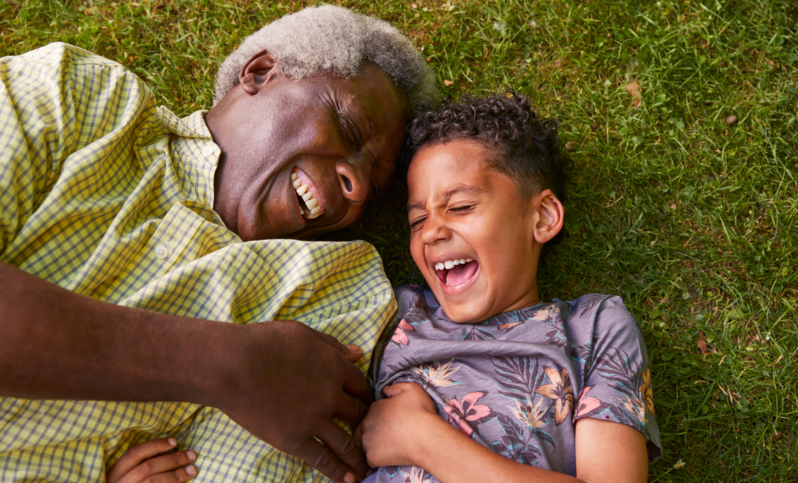 Grand-père allongé sur l'herbe avec son petit-fils et riant.