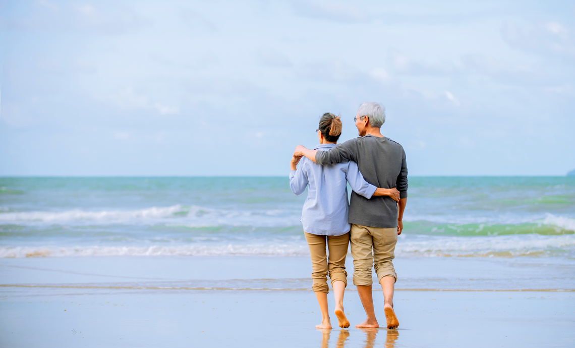 Older couple with arms around each other walking on a beach